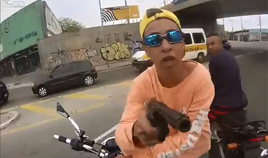 Młody bandyta grozi pistoletem motocykliście